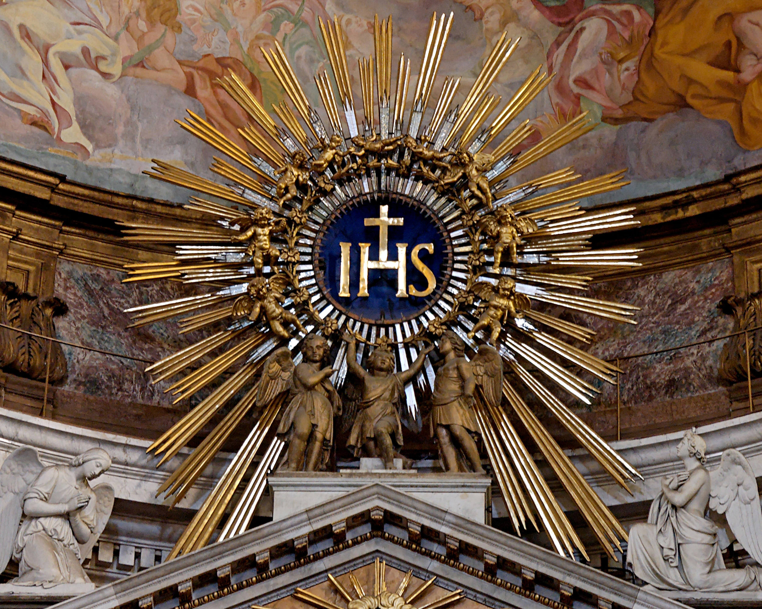 IHS monogram, on top of the main altar of the Gesù, Rome, Italy. Wikimedia Commons.