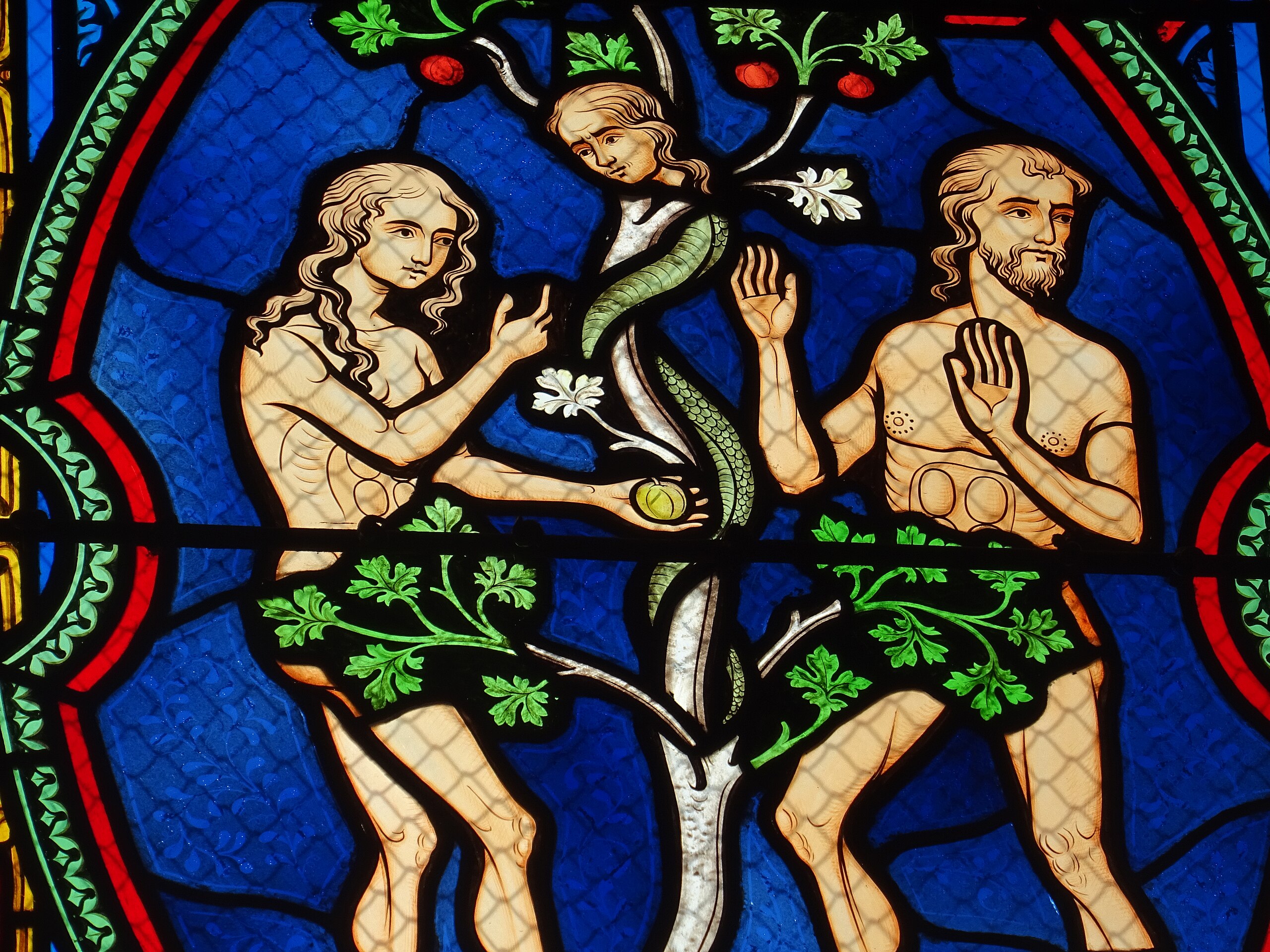 Adam and Eve with the Fruit and Serpent, in the Basilique Notre-Dame des Enfants. Stained glass, photographed by Olive Titus, 2020. Wikimedia Commons